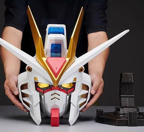 A person holds a large white, gold, and red Gundam-style robot head model against a dark studio background, with a black display stand visible to the right.