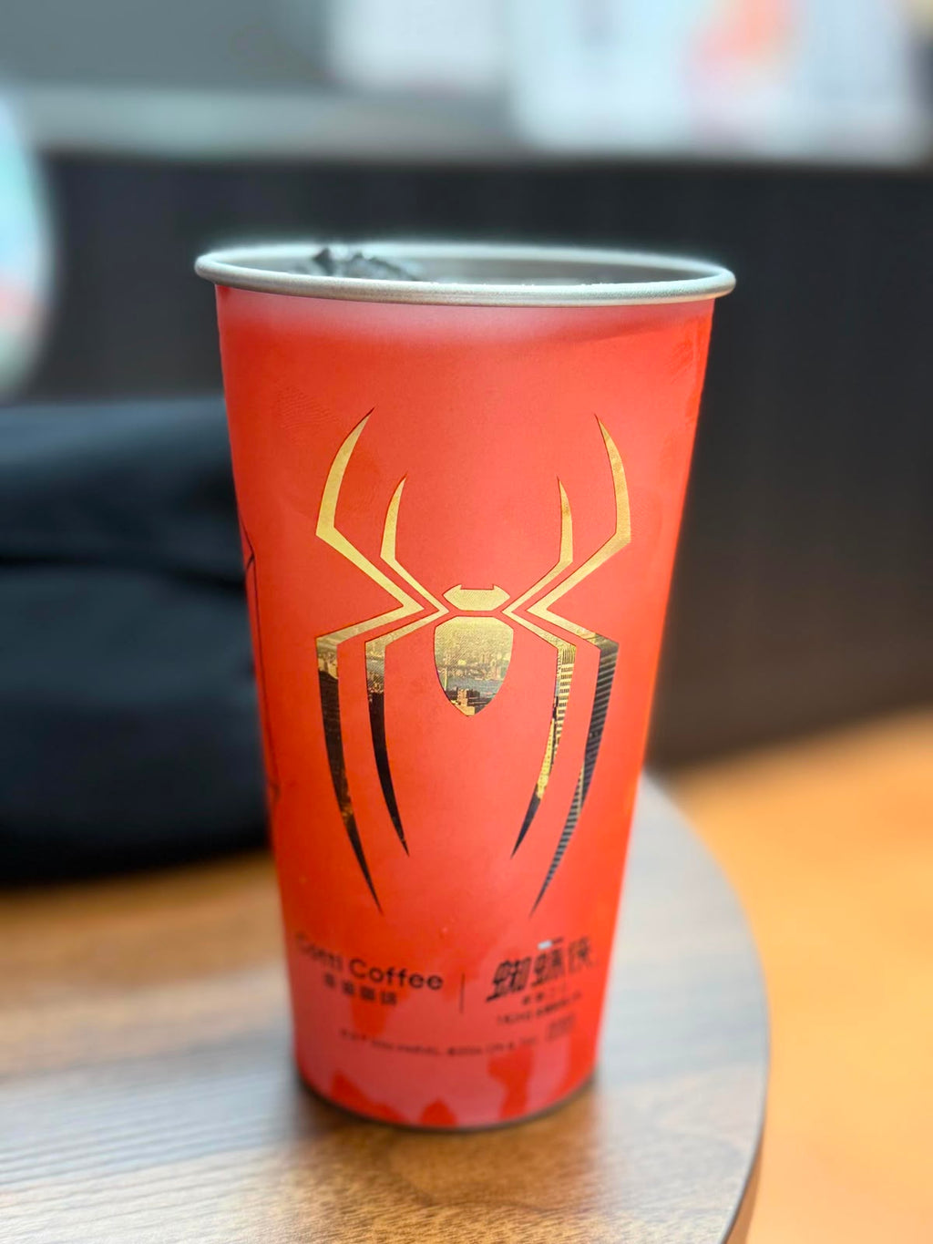 A red paper coffee cup with a gold spider graphic and Chinese text, sitting on a wooden table.