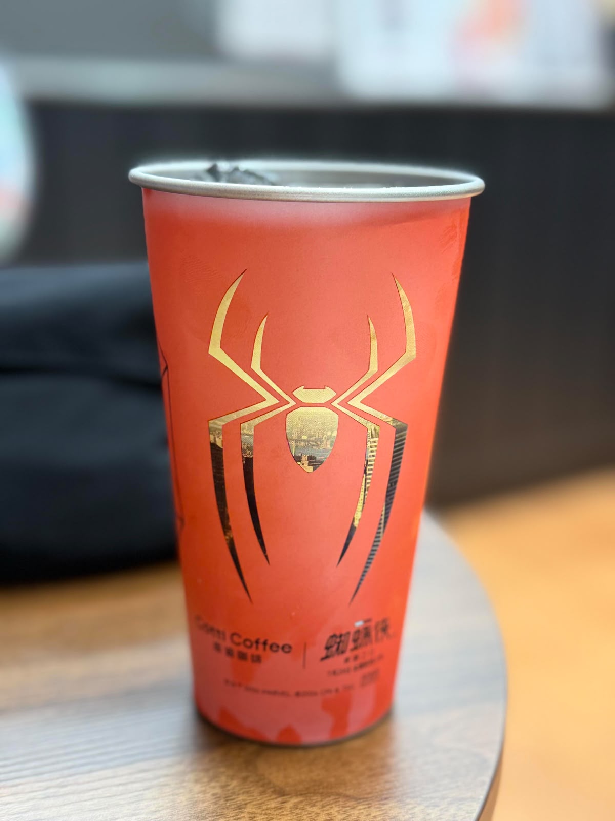 A red paper coffee cup with a gold spider graphic and Chinese text, sitting on a wooden table.