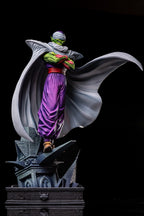 A detailed collectible statue of Piccolo from Dragon Ball Z, standing on a dark gothic pedestal with his cape dramatically spread, set against a solid black background.