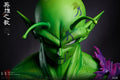 A close-up collectible figure of the Dragon Ball Z character Piccolo, shown from the chest up against a dark studio background. The figure has a bright green skin tone, pointed ears, and a small purple flower detail on the right side of the frame.