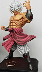 A detailed anime figurine of a muscular male character with spiky white hair, wearing a pink sash, white pants, and dark arm/leg guards, posed on a display base next to another collectible figure.