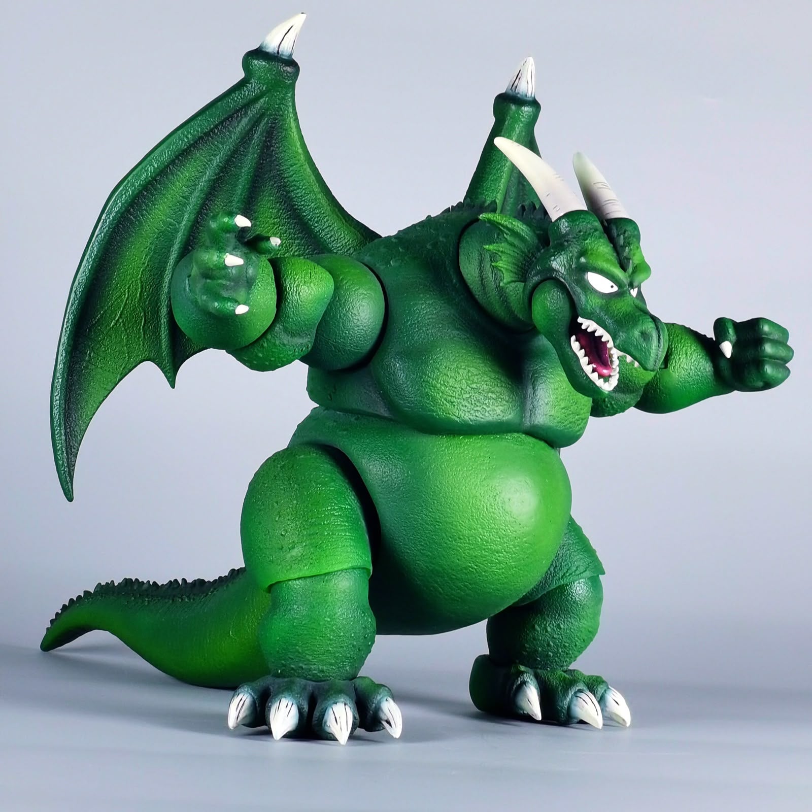 A green dragon action figure with white horns, large wings, and an open mouth showing white teeth, posed against a plain light gray studio background.