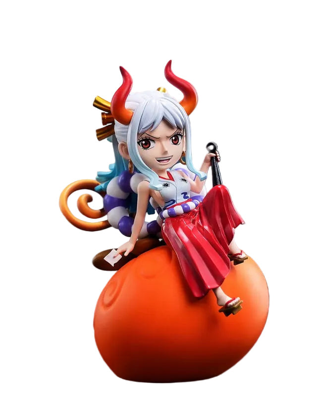 A One Piece Happy Life collectible figurine of a character with white hair, red horns, and a red dress, posed on an orange spherical base on a dark tabletop with a blurred cafe background.